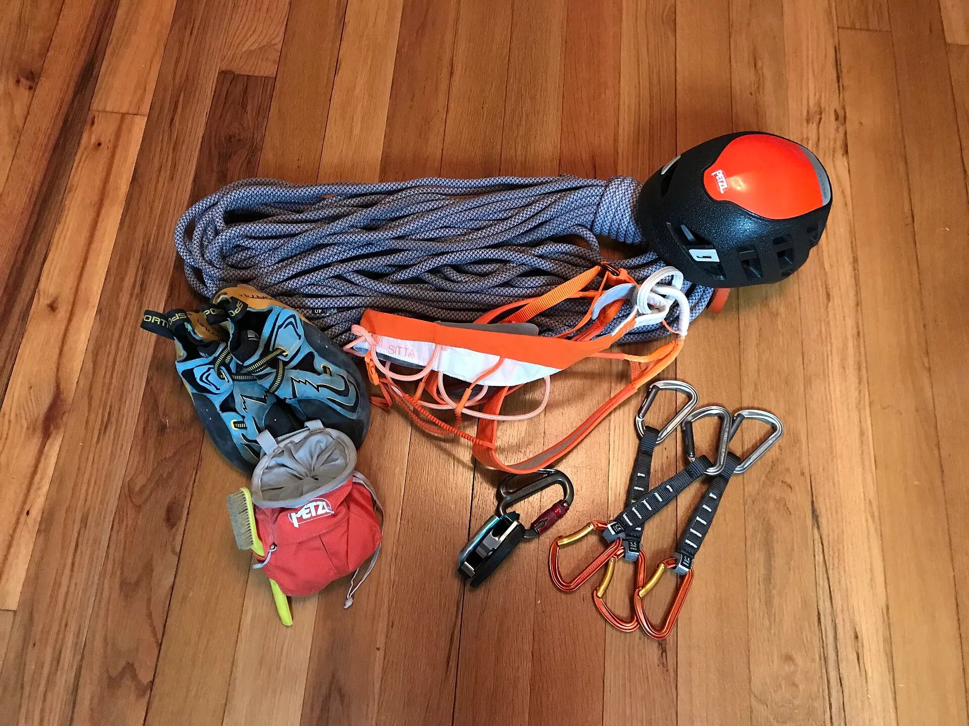 A rope, harness, helmet, shoes and quickdraws laid out on a wooden floor