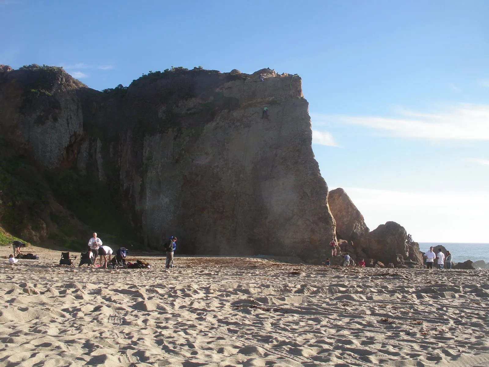 Climbers on the sand at the base of the Point Dume bluff, one climber high on the wall